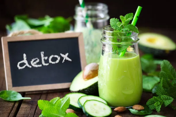 Bocal de jus vert à la menthe entouré d'avocat, de concombre et d'épinards, à côté d'une ardoise portant le mot « detox ».